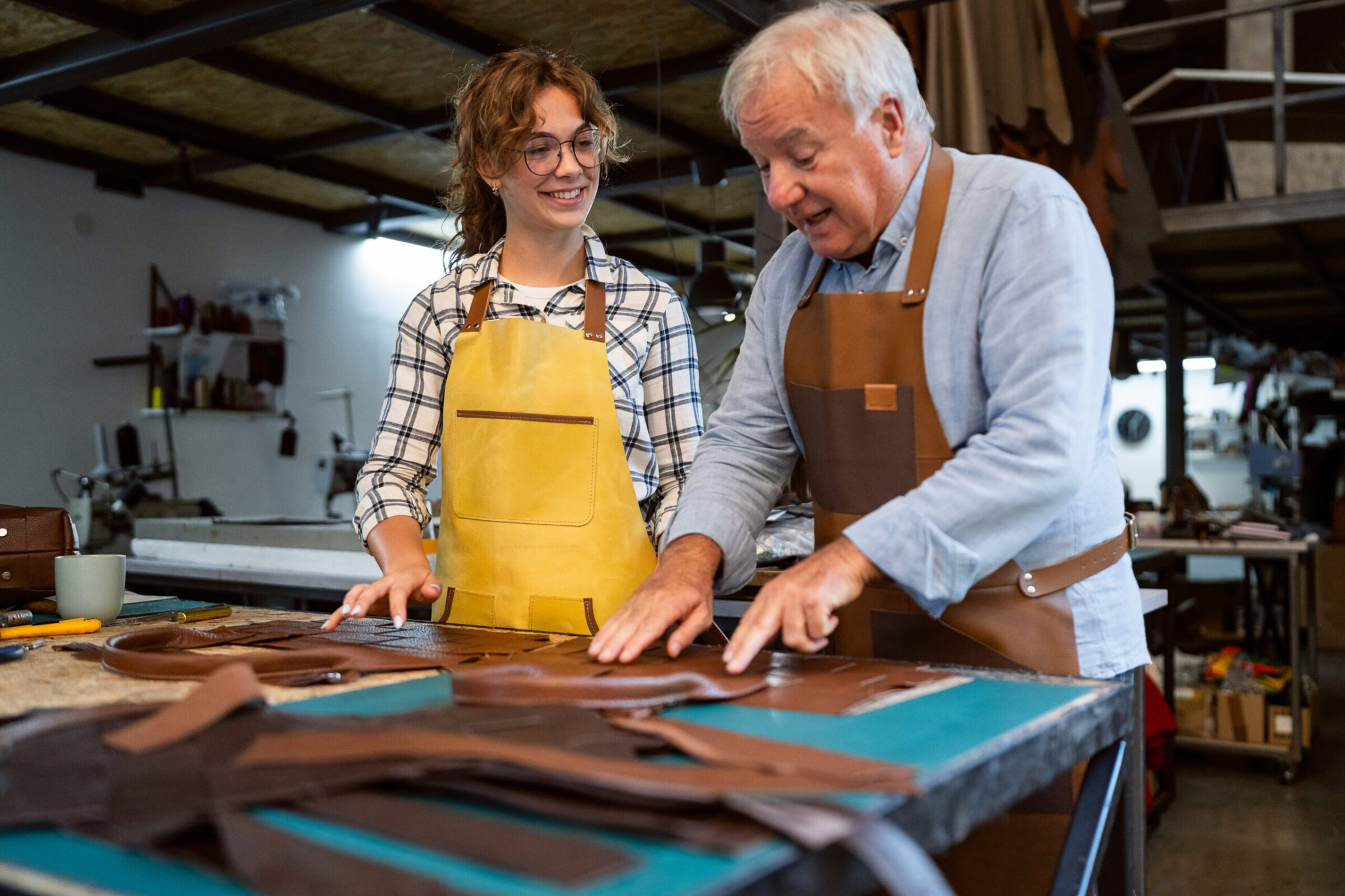 Senior craftsman teaching young apprentice in a leather workshop Agenzia per il lavoro AxL Leather